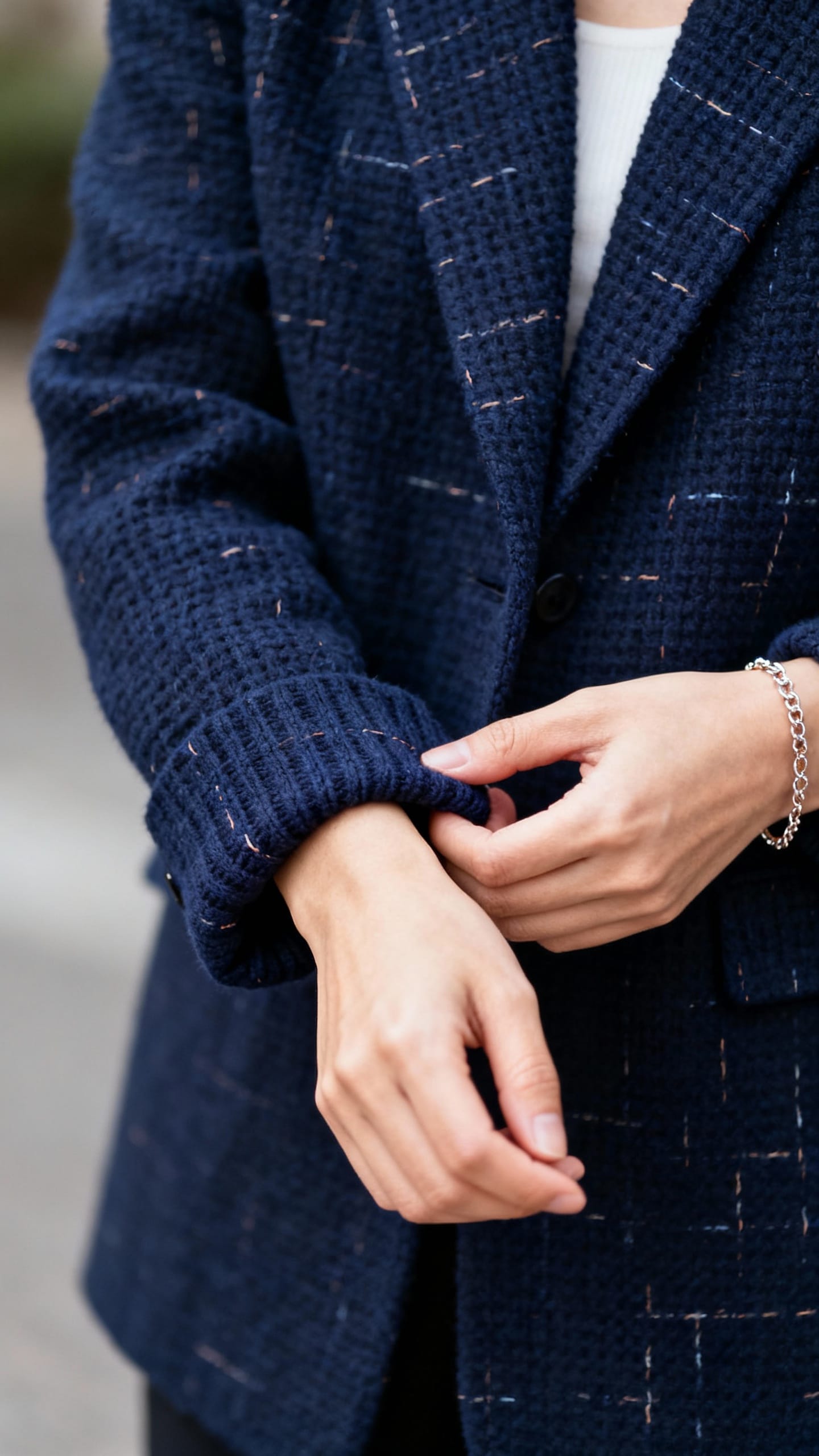 Closeup of female hands rolling blazer sleeves, bracelet showing, navy knit texture