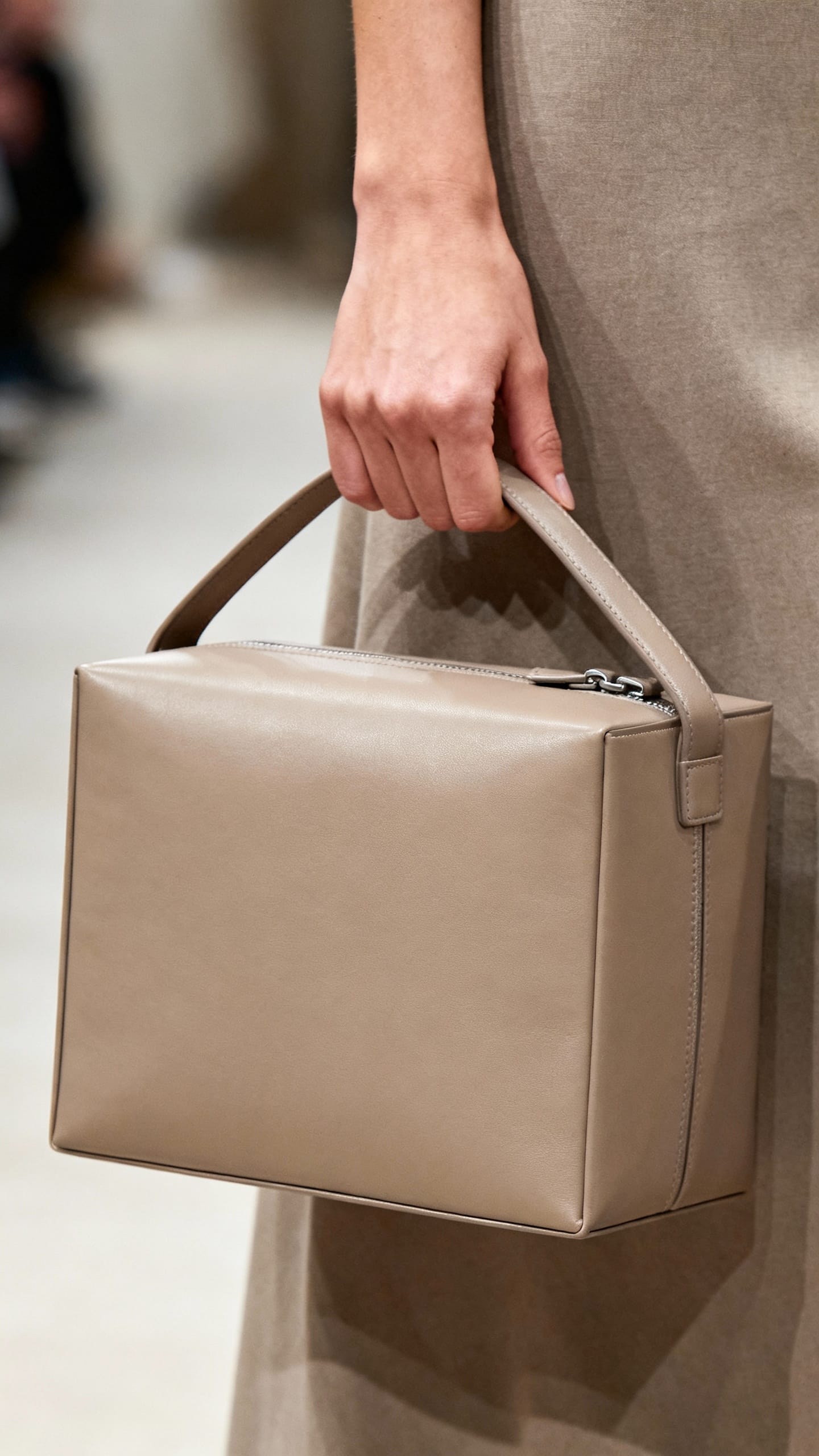 Female hand holding structured boxy leather bag, clean hardware