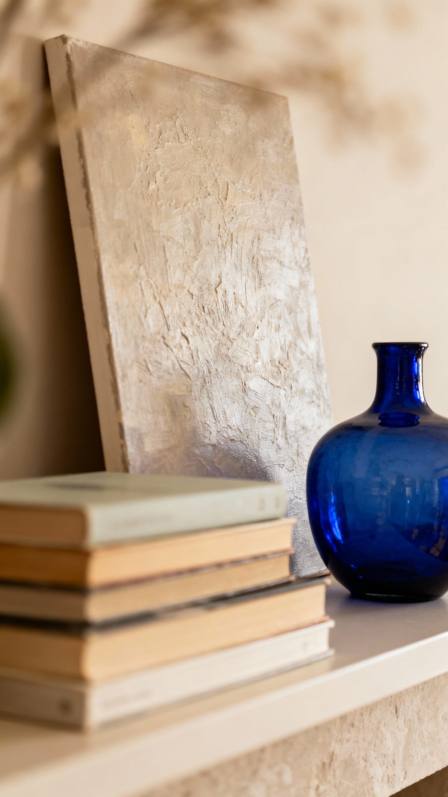 Layered shelf: leaning art backdrop, book stack, cobalt vase accent