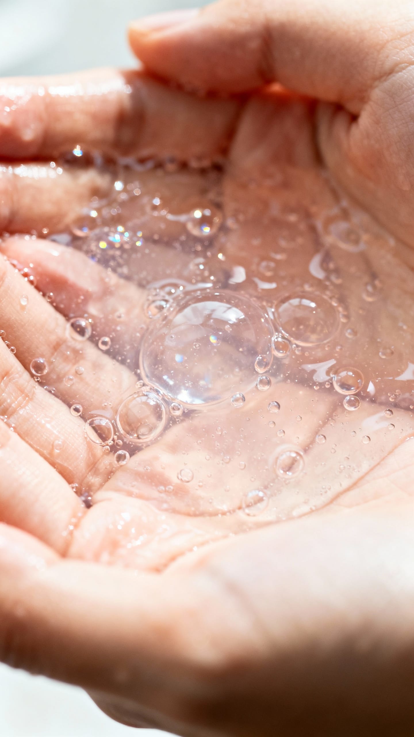 Hands applying gentle gel cleanser, close-up, water droplets
